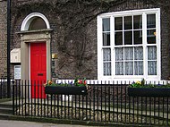 Colour photograph of the front of 23 Kirkgate in Thirsk. There are three storeys, two bay windows, and two stone steps leading to the entrance on left. This was the fictional Skeldale House in the James Herriot books and series. The building is now The World of James Herriot museum.