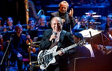 Hans Zimmer (composer of the 2021 film No Time to Die) with the Royal Philharmonic Orchestra at the Royal Albert Hall in London in 2022 during The Sound of 007 in Concert to mark 60 years of the Bond series. Sound007RAH041022 (42 of 69) (52406381295).jpg