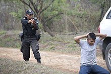A Guatemalan Policia Nacional Civil officer holding a suspect at gunpoint during a security checkpoint exercise. Due to the monopoly on violence held by the state, the police officer is allowed to use violence legally, while the suspect is not. A Guatemalan police officer, who is part of the Guatemalan Inter-Agency Border Unit, points his weapon at a simulated suspect to contain him during a vehicle checkpoint exercise at the Guatemalan military 130521-A-CL600-120.jpg