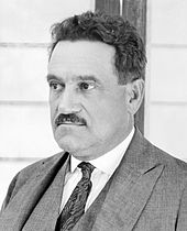 Black and white photo of a white man with a mustache, wearing a suit.