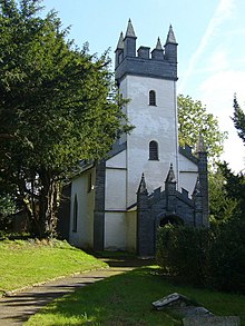 white-painted church with white tower that has castellated and turreted grey top standing in grassy area with trees