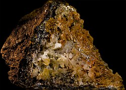 Bloc de roche brun cassé. L'intérieur révèle des cristaux blancs et jaunes avec des reflets métalliques gris ou jaunes.