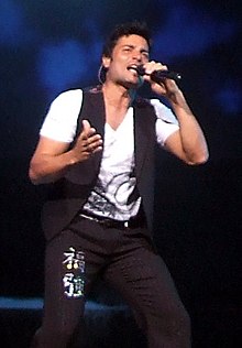 A young man with a microphone singing in a concert.