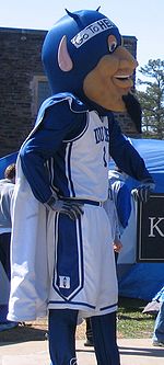 Duke Blue Devils mascot leans against sign with tents in background