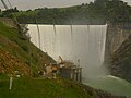 Englebright Dam during spring floods. Water is spilling over the dam's crest. Narrows II Powerhouse is visible at the base of the dam.