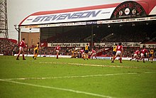 Photo datant de 1991 d'un terrain de football durant un match, une tribune latérale couverte en arrière-plan