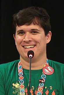 Chuggaaconroy is seen at PAX West 2018, speaking into a microphone and smiling.
