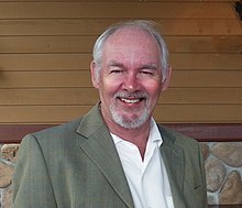 A medium, head and shoulder shot of a smiling white-haired Caucasian male with goatee and sports jacket on.