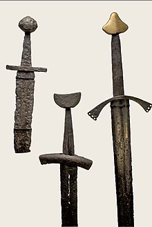 Farbfotografie von drei mittelalterlichen Schwertern. Beim linken Schwert fehlt die Spitze und der rechte Schwertknauf ist Gold.