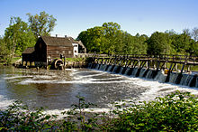A large river flowing from a spillway; a mill in the background
