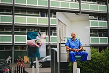 A photo with a block of flats in the background, and in the foreground signs like estate agent signs, except they show portrait photographs of people instead of 'for sale' posters.