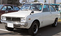 Un automóvil Mazda 323 (Familia Mk. 2/Rotary Coupé en Xapón) modelu 1969 nun aparcamientu.
