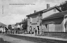 Carte postale noir et blanc avec le bâtiment voyageurs et sa halle accolée vu du quai opposé. Devant le bâtiment des perssonnages et à gauche une diligence à cheval
