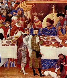 Les molt riques hores del Duc de Berry, gener (detall), c1410. els dos cortesans dempeus darrere de la taula a l'esquerra vesteixen caperons de confecció elaborada.