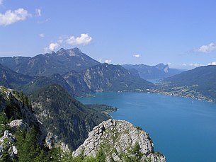 Gemeindegebiet Unterach: Mitte links, am Attersee, die Ortschaft, dahinter die Ortsteile Au/See am Mondsee, rechts Burgau am Attersee (St. Gilgen). Blick vom Schoberstein (1037 m, Höllengebirge), nach Westen gegen Schafberg (links, 1782 m) mit Ackerschneid und Kienbergwand (Mitte) und Drachenwand/Schober (rechts) sowie Hochplettspitz (ganz rechts)