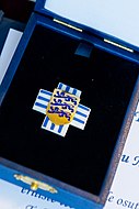 Photo d'un écusson bleu et blanc en forme de croix. Au centre, un blason : d'or aux trois lions azur