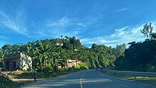 A road through a green hilly landscape in Bushenyi District.jpg