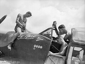 Two men sitting in and beside the cockpit, and another sitting astride the nose, of a military aircraft