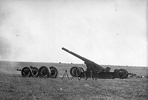 A large gun on its firing plate pointing to left in open ground. A wheeled carriage is nearby.