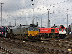 Zwei Crossrail-Diesellokomotiven in unterschiedlichen Farbvarianten. Vorn in silber-gelb eine Class 66, dahinter in roter Lackierung eine Class 77, die sich von der Class 66 durch die Klimageräte über den Führerständen gut unterscheiden lässt.