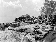 uneven beach in foreground littered with equipment, soldiers and amphibious vehicle in the distance