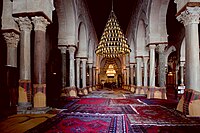 Photographie de la nef centrale de la salle de prière. Plus large et plus haute que les seize autres nefs, elle mène au mihrab. Elle est bordée, de part et d’autre, d’une double ligne d’arcades à colonnes géminées.