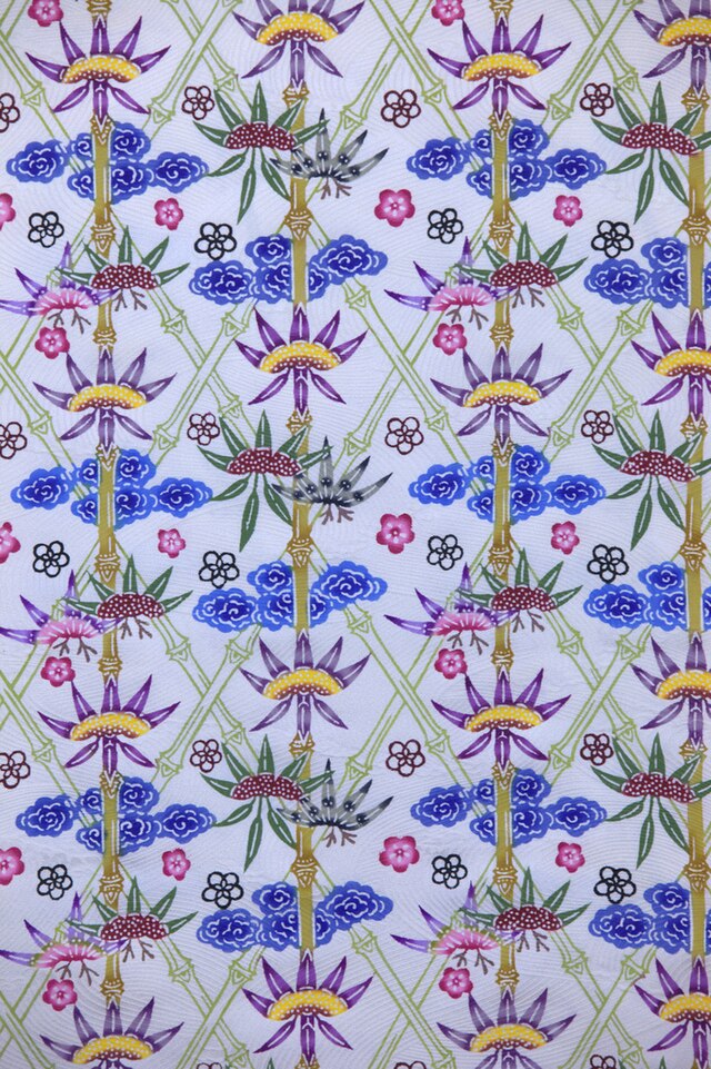 Fabric decorated with a busy design of diamonds constructed from light green bamboo stems and blue, pink and purple flowers on a white background.