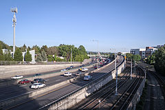 Photograph of a section of rail tracks next to a freeway exit ramp with busy a six-lane freeway to the left