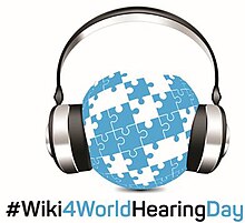 Globe formed of light blue puzzle pieces. The globe is enclosed by silver and black headphones. A hashtag below the image reads Wiki 4 World Hearing Day.