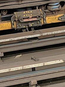 The contact shoe of a New York City Subway car making contact with the third rail. In the foreground is the third rail for the adjacent track. NYC Subway Third Rail Induction Motor.jpg