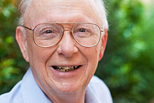 A smiling man with white hair wearing bifocals
