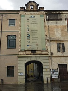 Imatge de l'arc que fa d'entrada principal a la Factoria Cultural Coma Cros de Salt. De la façana en penja una pancarta amb un seguit d'institucions i entitats que tenen local o seu dins el recinte