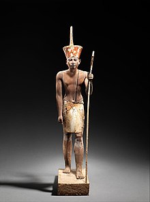 A figure wearing the red crown of Lower Egypt and whose face appears to reflect the features of the reigning king, most probably Amenemhat II or Senwosret II. It functioned as a divine guardian for the imiut, and it is wearing a divine kilt, which suggests that the statuette was not merely a representation of the living ruler. GuardianStatueofAmenemhmatII.jpg