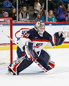 A female ice hockey goaltender is on the ice. She is standing with her knees bending.