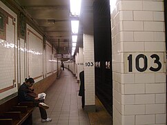 View of a narrow section of the southbound platform. There is a bench and wall to the left, as well as pillars with the number "103" to the right. There are subway tracks to the far right.