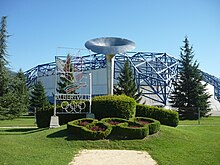 La halle olympique en fond ; devant, une sculpture de vasque olympique et une sculpture d'anneaux olympiques et l'inscription "Albertville".