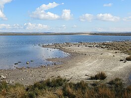 A sandy, rocky foreshore with water beyond, and an upland horizon