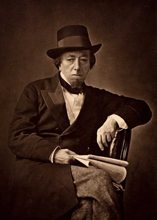 Disraeli in old age, wearing a double-breasted suit, bow tie & hat