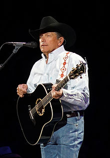 A man standing, wearing a hat, playing a guitar.