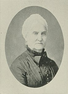 B&W oval portrait photo of a white-haired old woman wearing a dark blouse.