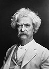 A hazy photograph of Mark Twain, with white hair and mustache in a light-colored suit