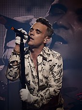 Photograph of Robbie Williams singing into a microphone while closing his eyes
