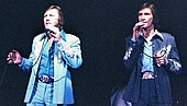 A picture of two men dressed in blue colors singing at a concert.