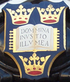 A shield displaying a coat of arms; on a dark blue background, an open book displays the words "Dominus Illuminatio Mea"; two gold crowns above, one below