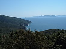 Paysage avec au premier plan des collines boisées qui tombent dans un golfe, et à quelque distance une île.