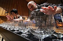 Photographie en couleurs montrant un homme manipuler une multitude de verres placés les uns à côté des autres en plusieurs rangées.