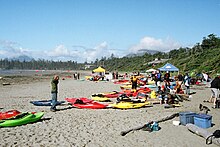 Photo of beach, with several kayaks strewn around and people in background