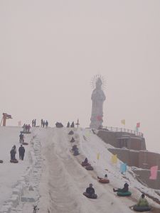 People sporting in snow by a statue of goddess Guanyin in Wujiaqu