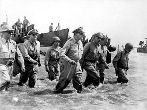 A group of men wading ashore. With General MacArthur is Philippine President Sergio Osmena and other US and Philippine Generals.
