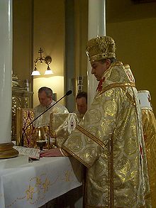 A bishop celebrating Divine Liturgy in a Greek-Catholic church in Presov, eastern Slovakia. Another bishop stands to his immediate right (white omophorion visible), and two married priests stand to the side (facing camera). Jan Babjak SJ.jpg